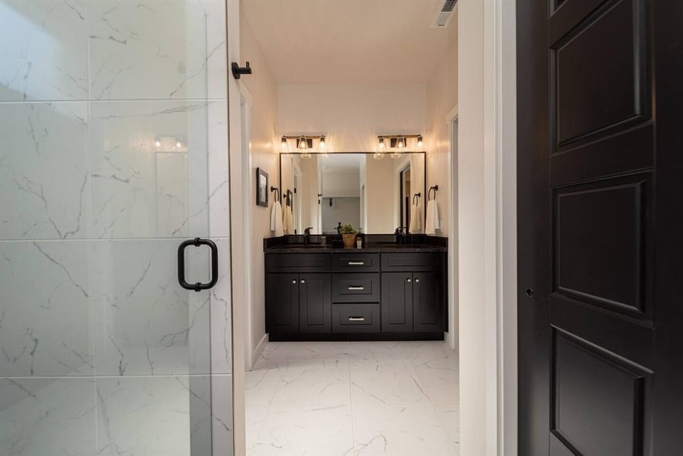 Spacious and luxurious bathroom featuring marble flooring, a large glass shower, and a dual vanity set against a rich, dark cabinetry