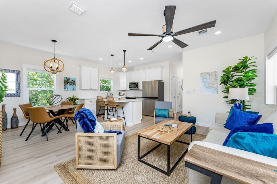 The open living, dining, and kitchen area in Unit 1A offers a bright coastal space with comfortable seating, a queen sofa sleeper, dining table, and a fully equipped kitchen with bar seating and stainless steel appliances.