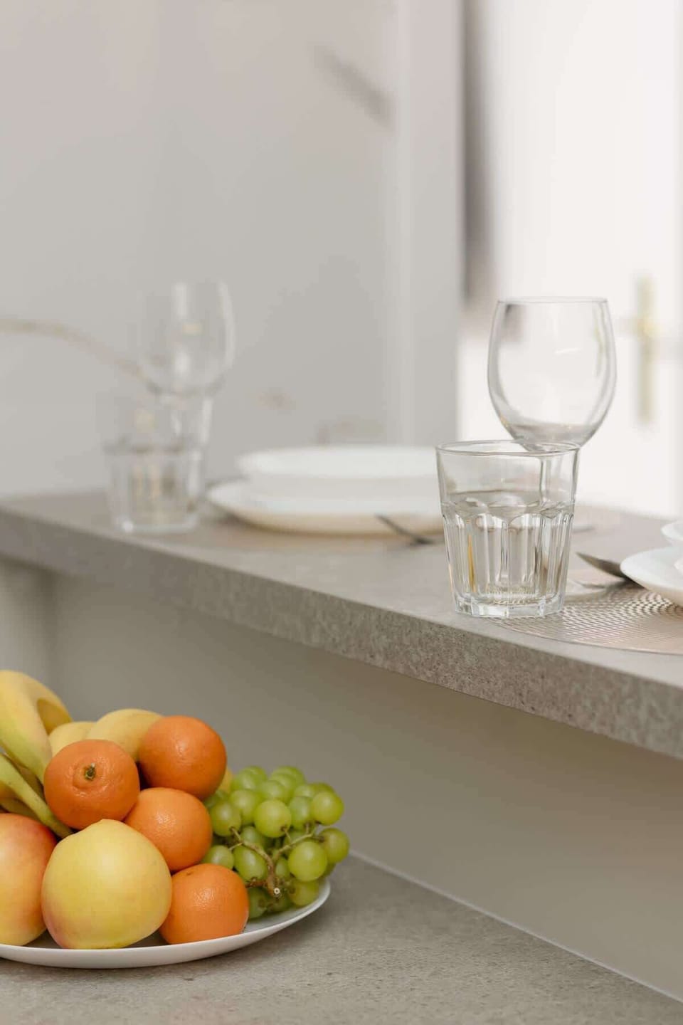Minimalist dining setup with a white table, fresh fruit, and sparkling glassware.






