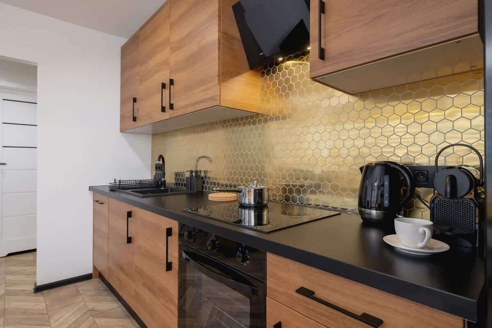 A stylish kitchen with wooden cabinets, black countertops, and a bold yellow backsplash, exuding a contemporary industrial vibe.
