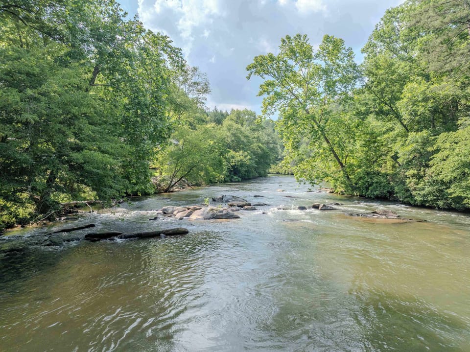 Experience the beauty of nature at its best — a serene river framed by lush greenery and dotted with natural rock formations, creating a picture-perfect spot for relaxation, exploration, or a quiet moment by the water.