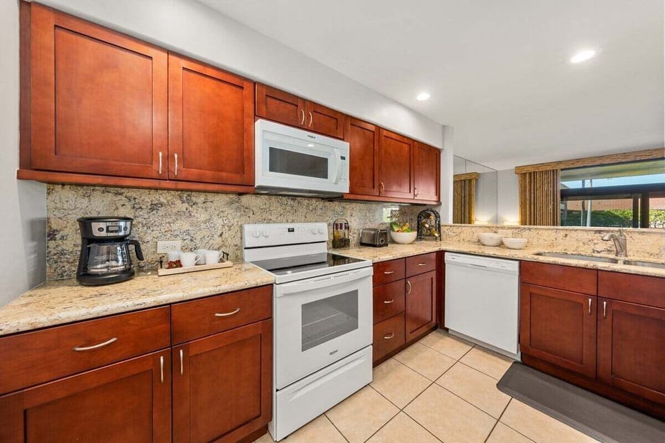 Fully equipped kitchen featuring granite countertops, rich wood cabinetry, and white appliances
