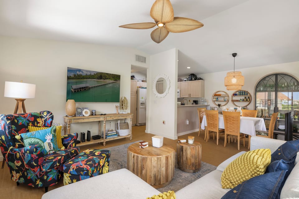 Unwind in your bright open-plan living space where tropical vibes meet modern comfort, featuring colorful furnishings and ocean-inspired art.