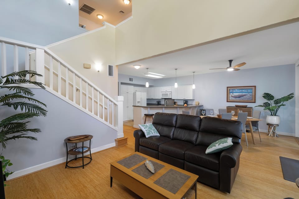 Unwind in your spacious open-concept living area with plush leather seating, warm hardwood floors, and tropical plants creating a welcoming atmosphere.