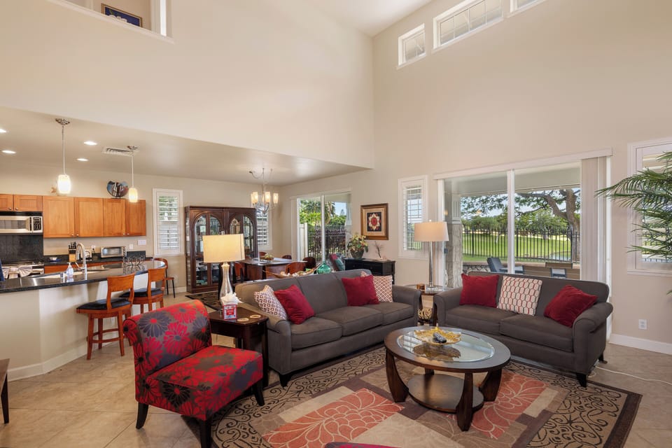Relax in your spacious open-plan living area with soaring ceilings, where plush gray sofas and vibrant red accents create the perfect setting for memorable evenings together.