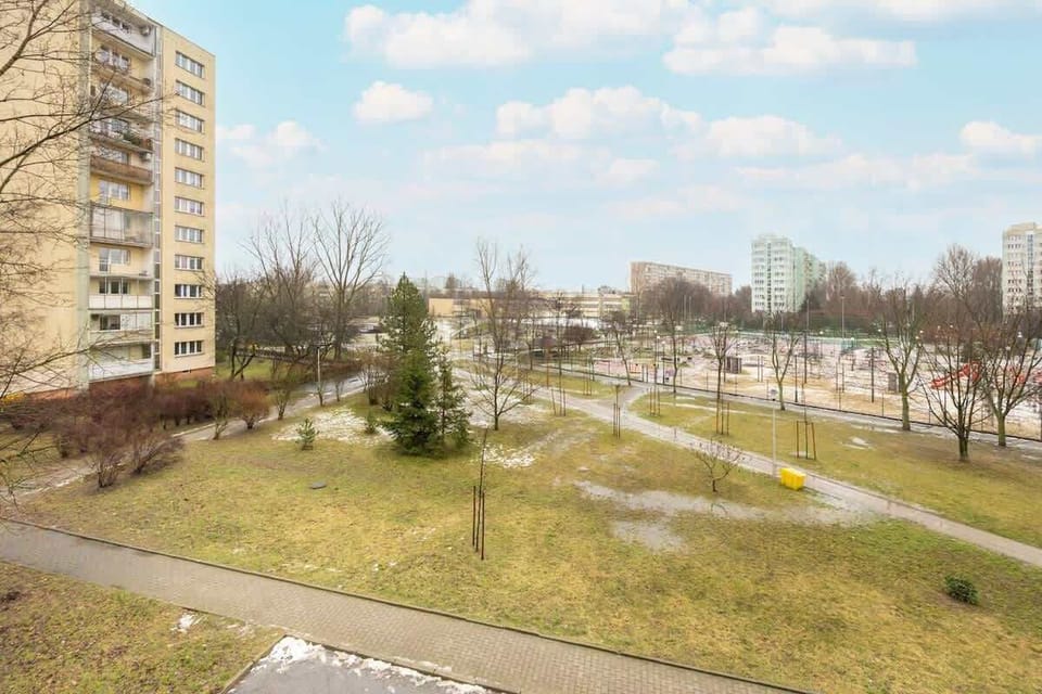A view of a well-maintained green space with walking paths, trees, and residential buildings in the background, creating a tranquil outdoor setting.

