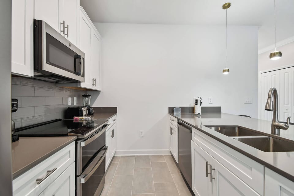Welcome to this stylish kitchen featuring sleek black granite countertops and crisp white cabinetry. Modern stainless steel appliances and pendant lighting create a chic, functional space, ideal for your culinary adventures.