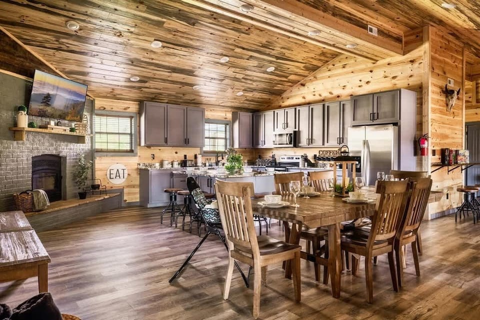 Rustic kitchen and dining area with wood-paneled walls and ceiling and a cozy fireplace.