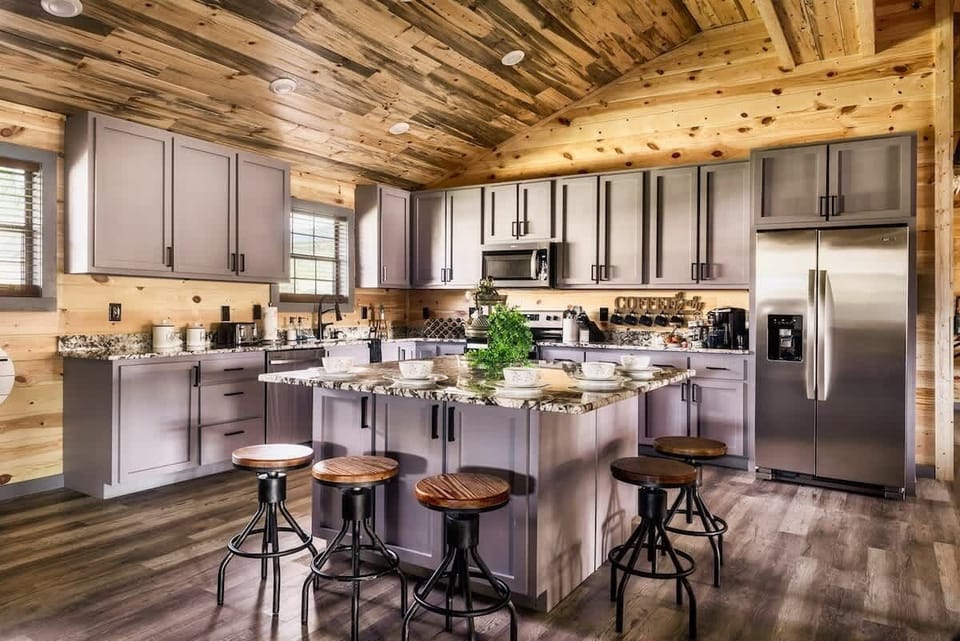 Modern kitchen with granite countertops and a large island surrounded by wooden stools in a rustic cabin setting.
