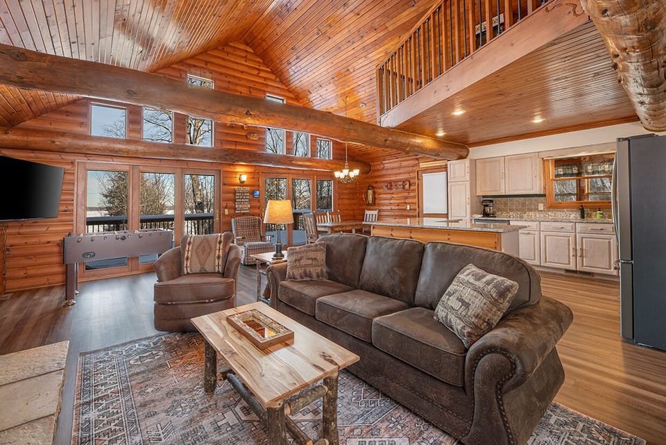 - Spacious living room with wood walls and tall ceilings - Foosball table adds fun for groups and families - Open layout connects kitchen seating and forest views