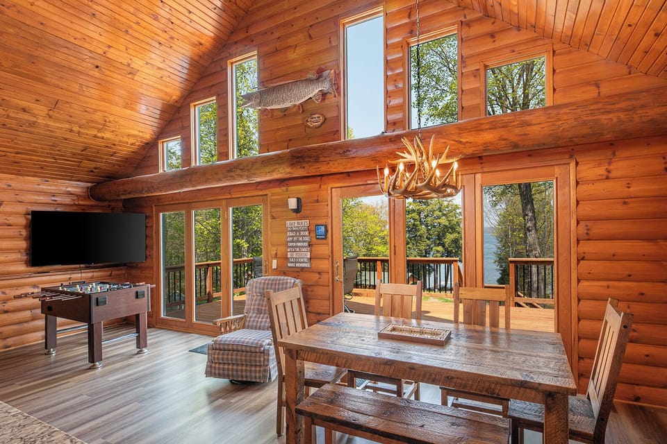 - Sunlit great room with tall windows and wood beam charm - Dining area opens to forest views and outdoor deck - Open layout blending comfort warmth and rustic style