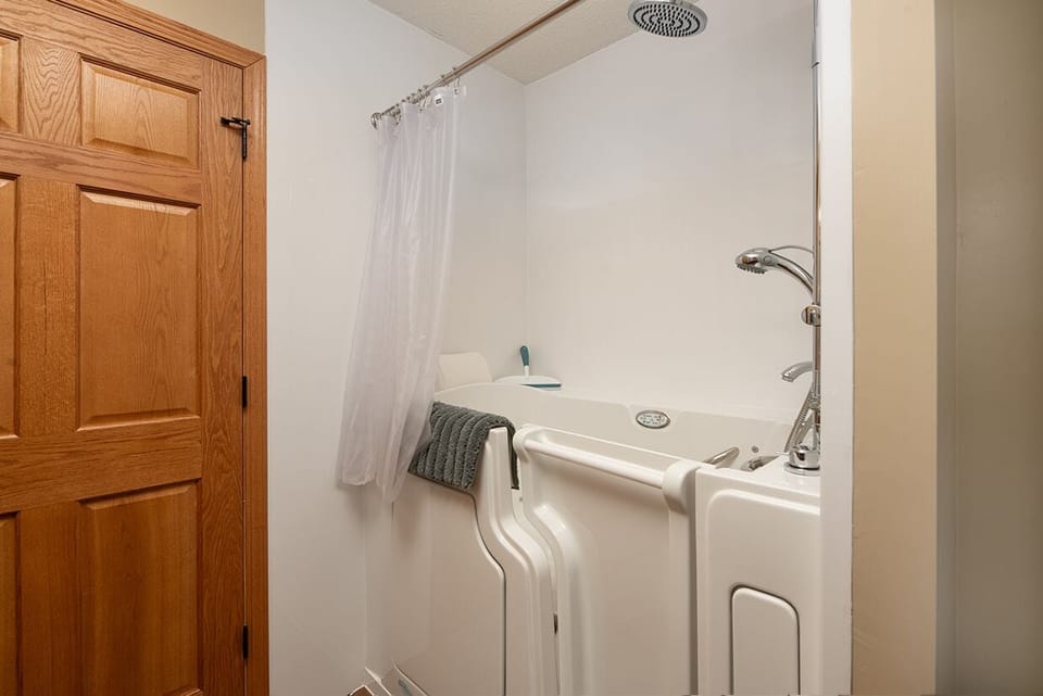 - Walk in tub with safety door and handheld shower sprayer - Clean bright walls create a simple functional setup - Comfort focused design perfect for guests needing easy access