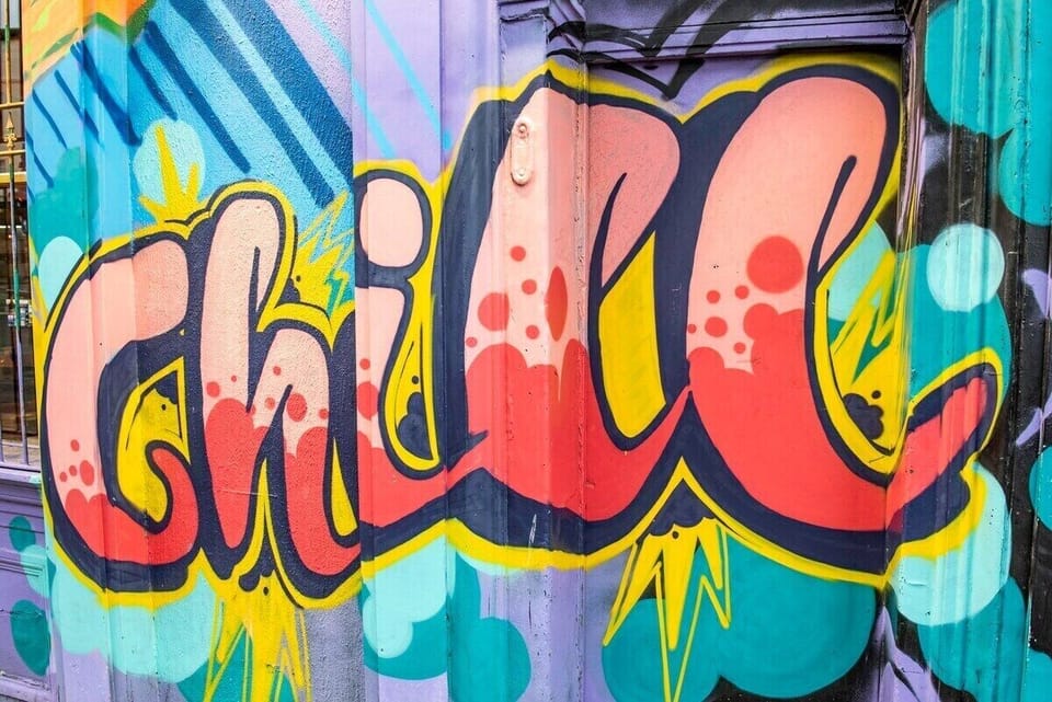 This striking street-art scene captures the creative spirit surrounding Camden Apartments. A bold mural featuring a vivid blue eye set within a pink triangle takes centre stage, framed by bursts of colour and contemporary graffiti lettering. Reflected perfectly in a rain-kissed pavement below, the image creates a dramatic mirror effect that feels effortlessly cool and unmistakably city-centric.