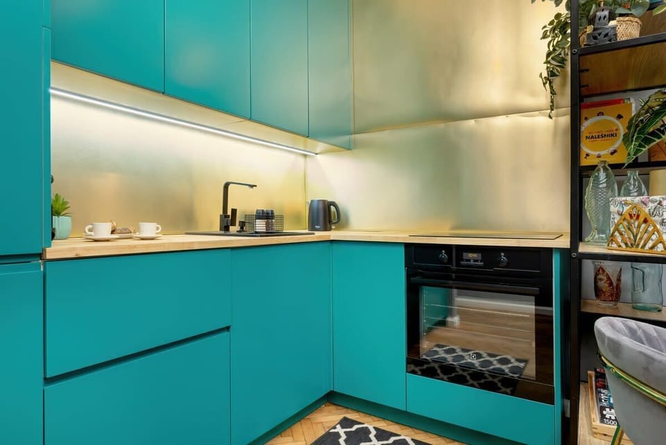 A compact kitchen with turquoise cabinets, under-cabinet lighting, and built-in appliances.

