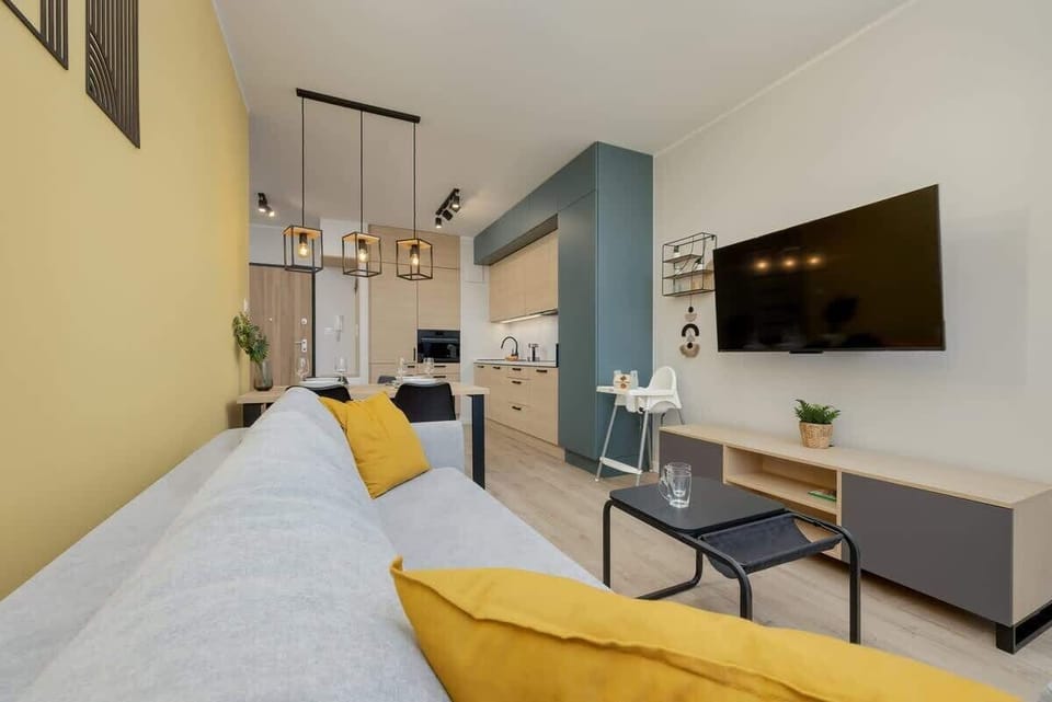 A cosy living room with a flat-screen TV in front of which you can spend pleasant evenings. In the background you can see the kitchenette connected to the living room by a dining table. 