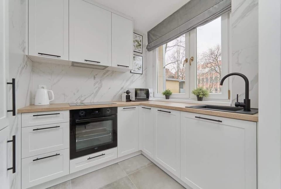 A sleek white kitchen with marble countertops, built-in appliances, and a large window.
