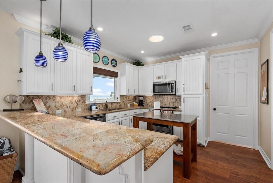 Fully equipped kitchen with granite countertops, white cabinetry, breakfast bar, stainless steel appliances and decorative pendant lighting.