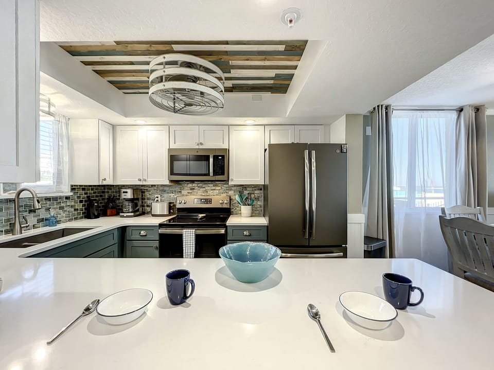 This well-equipped kitchen features a spacious island with seating, stainless steel appliances, and a unique wooden ceiling accent, blending comfort and style for a perfect gathering space.