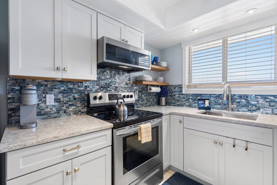 A kitchen with coastal charm, featuring glass-tile backsplash, quartz countertops, and plenty of natural light.