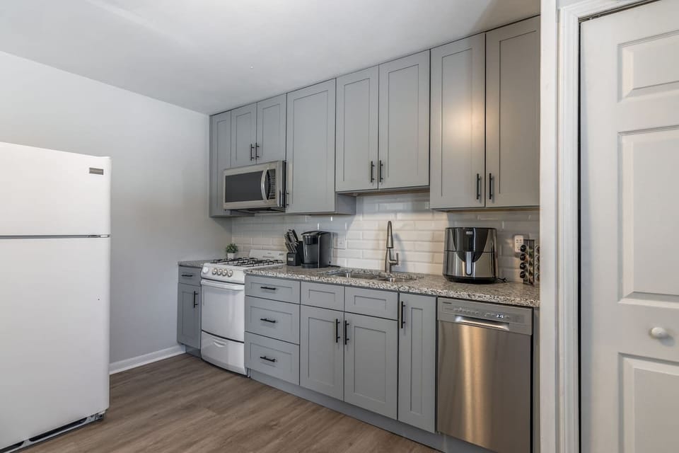 Modern galley kitchen with stylish gray cabinetry, stainless steel appliances, and granite-style countertops. Fully stocked for home cooking with microwave, dishwasher, and coffee maker…perfect for short or extended stays.