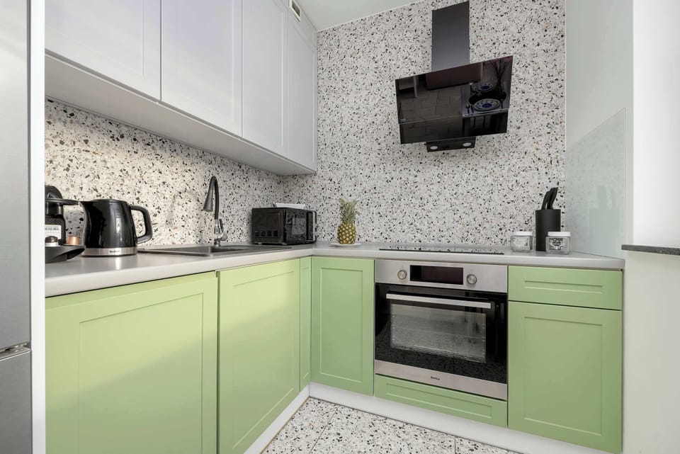 A modern kitchen with green cabinets, a patterned backsplash, and built-in appliances.
