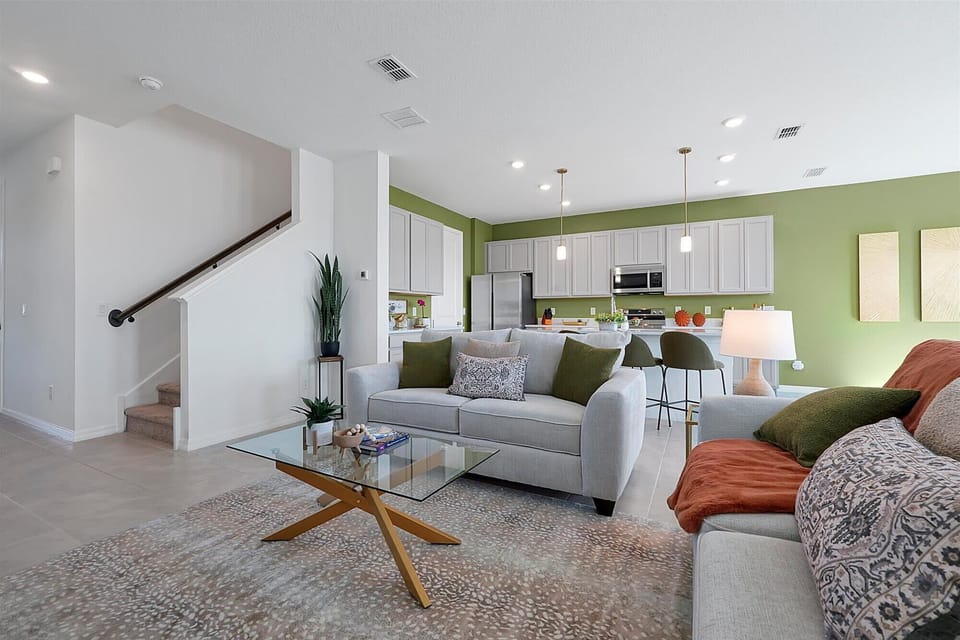 Airy living space w/ green accents, neutral seating & an open staircase.
