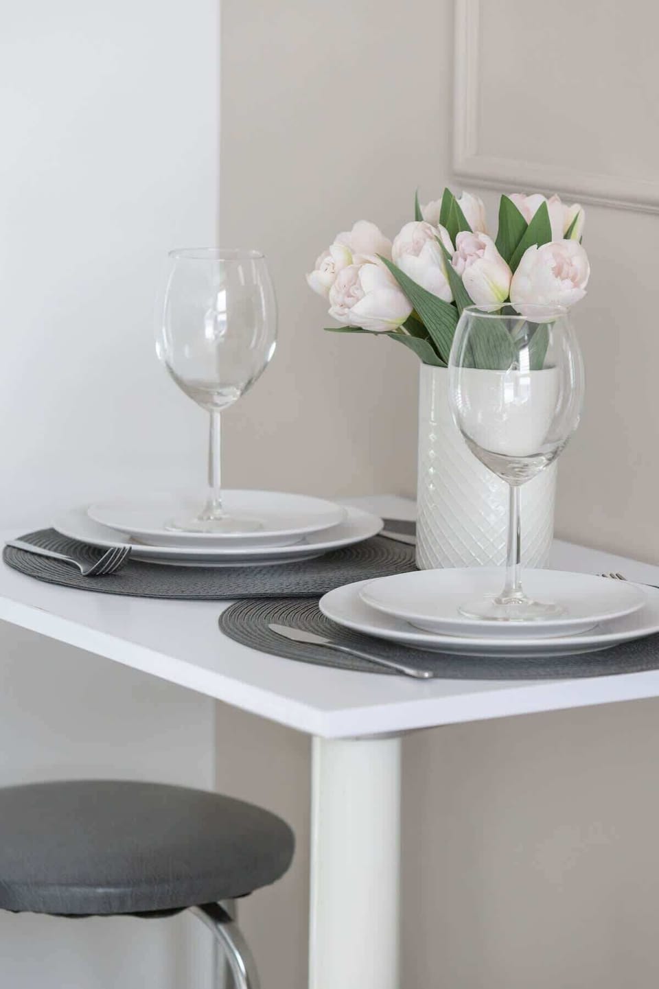 A small dining area with a white table, two stools, and a vase with fresh flowers for a cozy setup.
