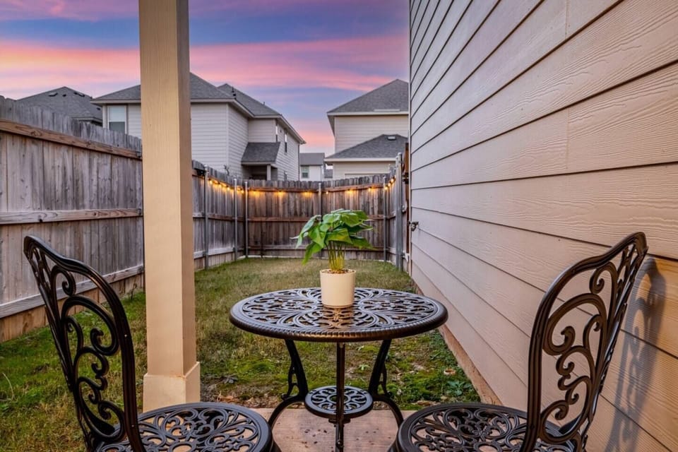 Cozy outdoor patio with charming seating for two, perfect for morning coffee or evening relaxation. The fenced yard provides privacy, and string lights add ambiance, making it an ideal spot to unwind during your stay. A peaceful retreat.