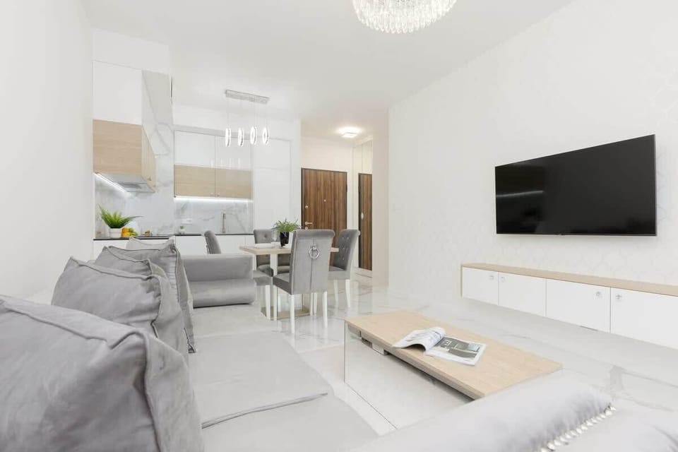A modern living room with grey sofas, a white entertainment unit, and minimalistic decor, creating a clean and airy look.
