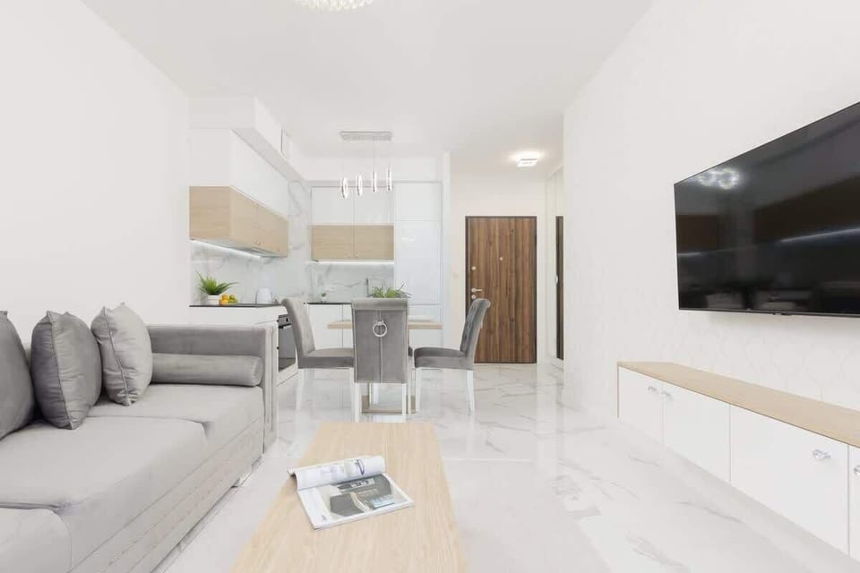 A spacious living area with a sectional sofa, minimalist decor, and an open kitchen concept, ideal for socializing and relaxation.
