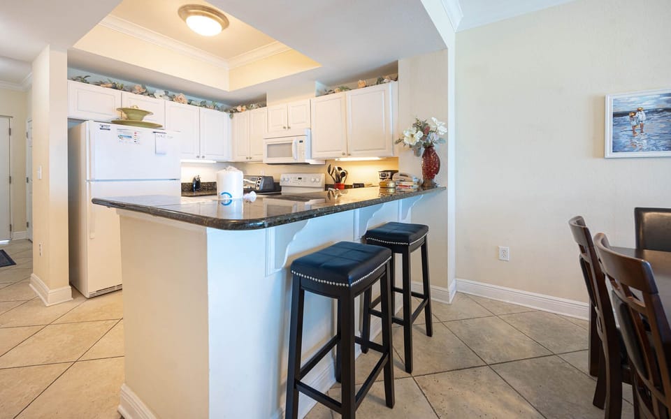The kitchen features white cabinetry, granite countertops, and a breakfast bar with stylish seating