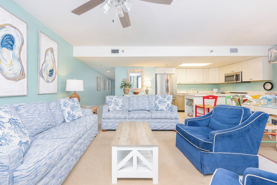 Living area features blue and white patterned sofas, a wooden coffee table, and a view into the modern kitchen space