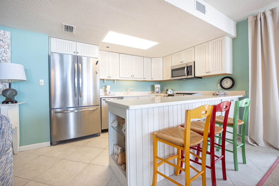 Kitchen area featuring a white countertop, colorful bar stools, and modern appliances against a soothing blue backdrop