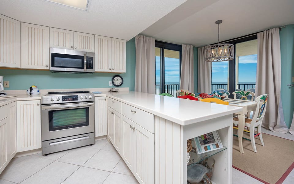 Brightly colored dining chairs surround a table in this kitchen, featuring a sleek countertop and views of the beachfront