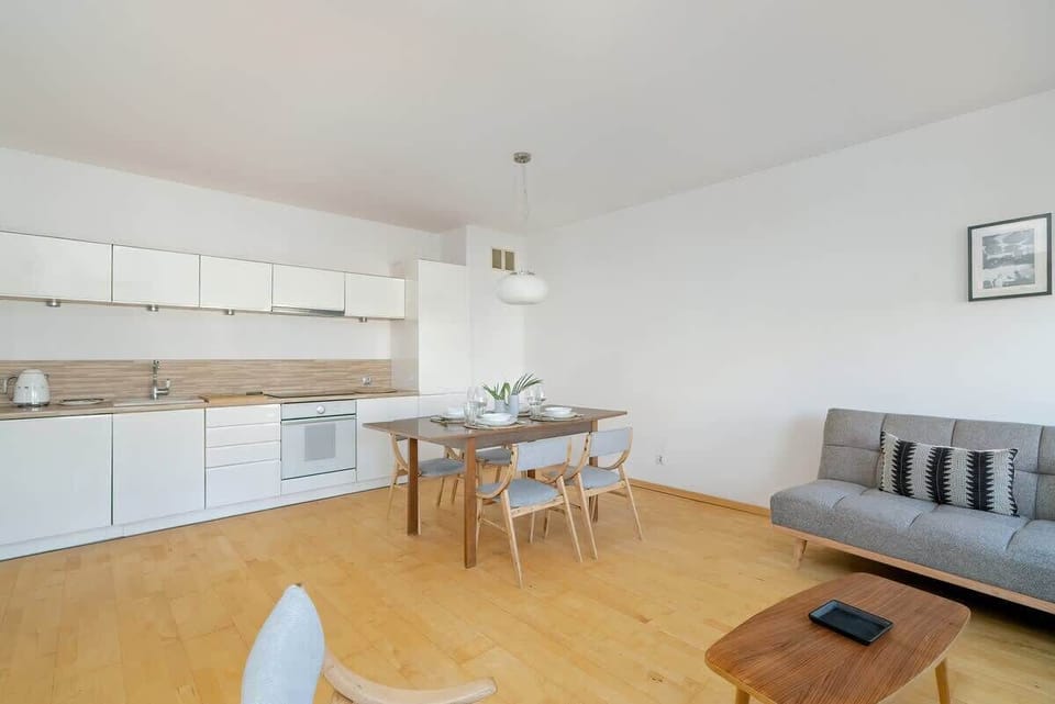 A full view of the kitchen and living space, featuring a functional layout with white cabinetry, wooden countertops, and stylish shelving.

