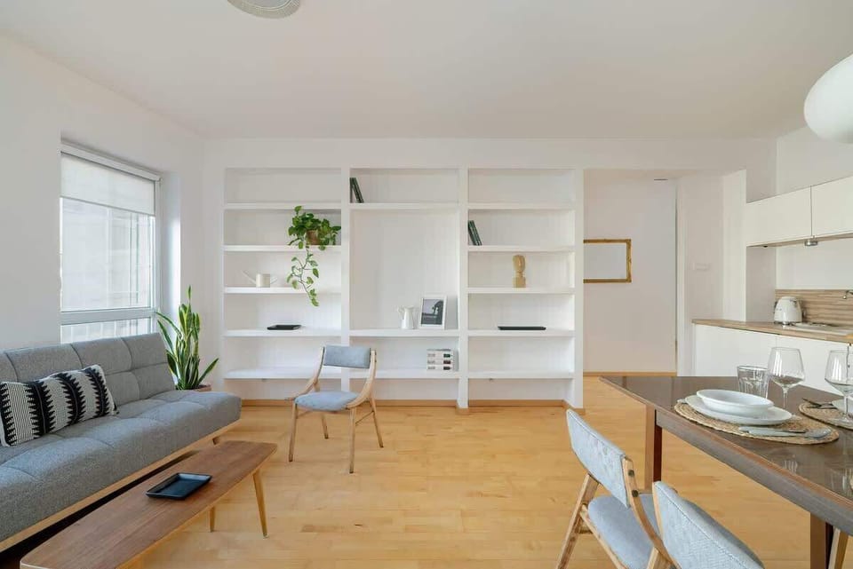 A wider perspective of the open-concept kitchen and dining area, showcasing white cabinets, floating shelves, and a bright, airy design.

