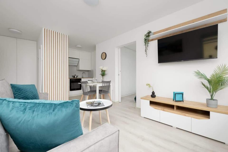 Another angle of the living room, featuring a wall-mounted TV, wooden accents, and a well-balanced neutral and teal color palette.

