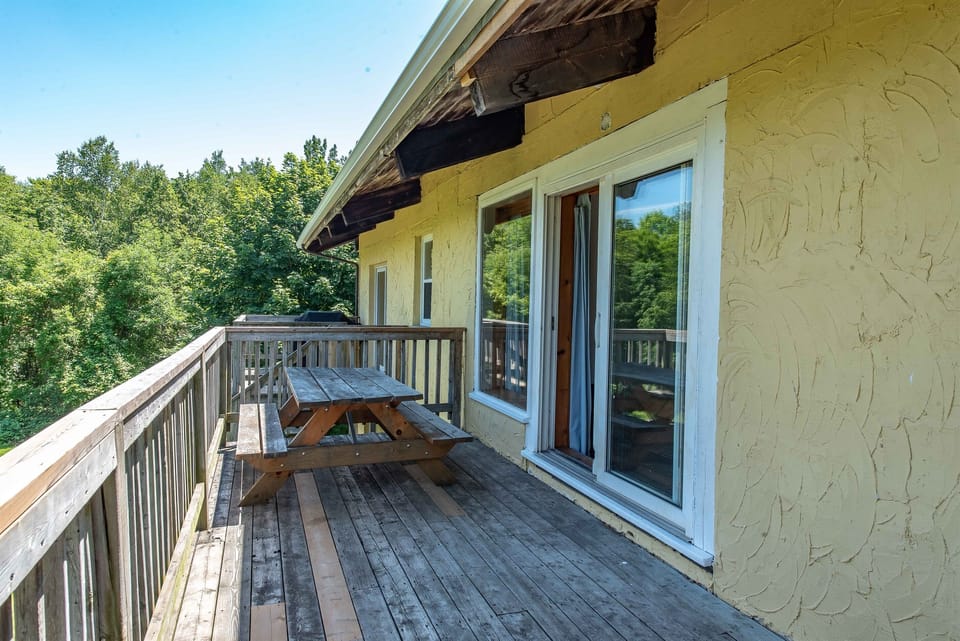 Oversize balcony for outdoor barbecuing and dining with view of backyard and forest
