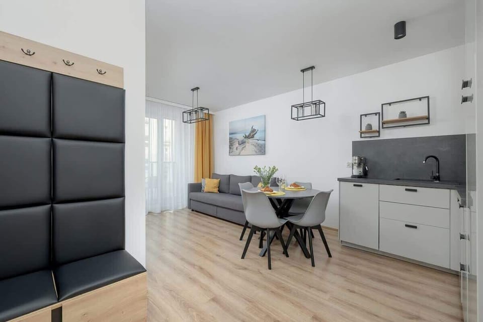 A view from the hallway into the apartment, highlighting a black upholstered wall panel and the open-concept kitchen and dining area.

