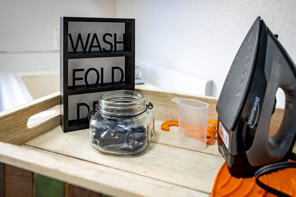 Laundry shelf with pods, scoop, and framed “Wash Fold Dry Repeat” sign.