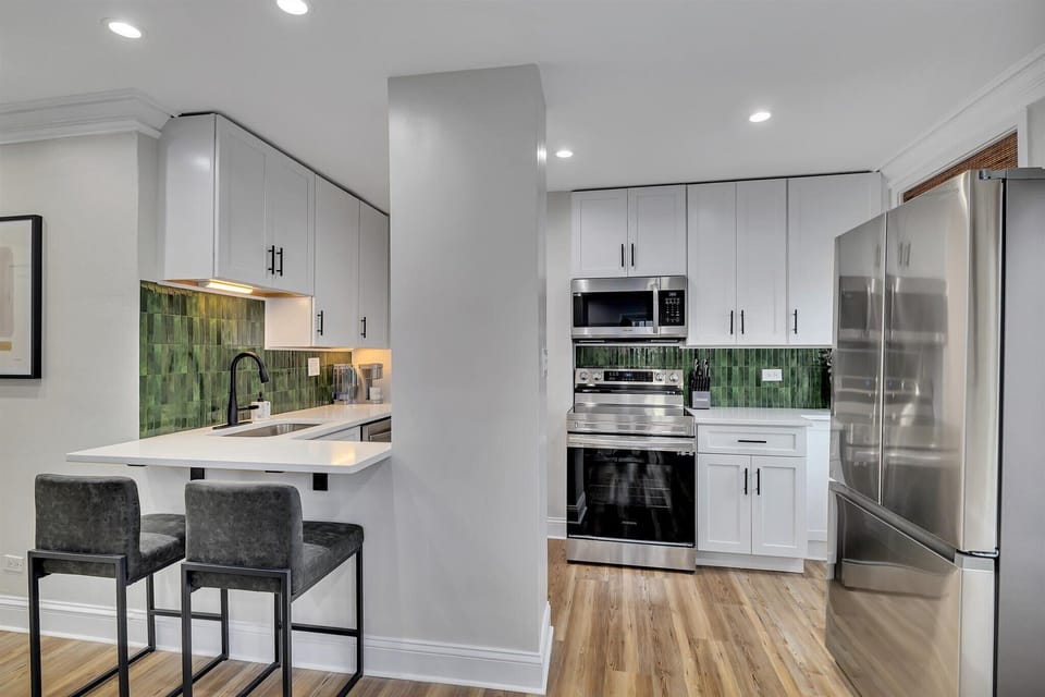 Sleek kitchen w/ modern appliances, green tile backsplash & bar seating for quick meals