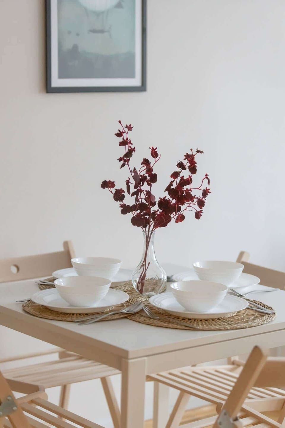 A detailed view of a dining table set with white plates, glasses, and a decorative vase with red flowers, enhancing the aesthetic of the space.







