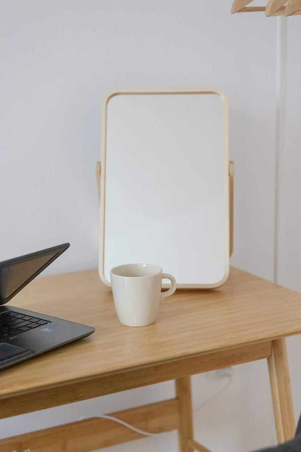 A simple wooden bedside table with a mirror and laptop, perfect for a small workspace or vanity area.

