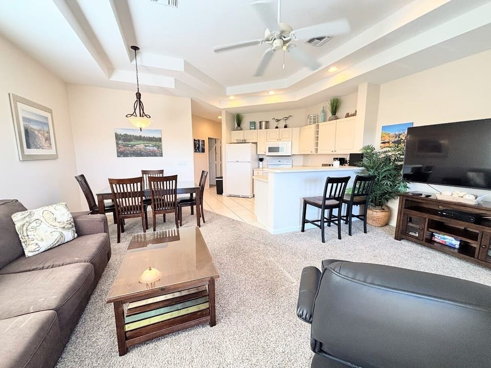 Spacious open-concept living and dining area with high ceilings, comfortable seating, breakfast bar, and a bright kitchen layout.