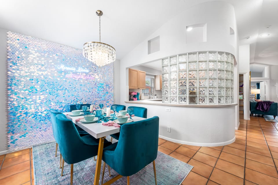 Chic setup in he dining area featuring teal chairs and a shimmering accent wall