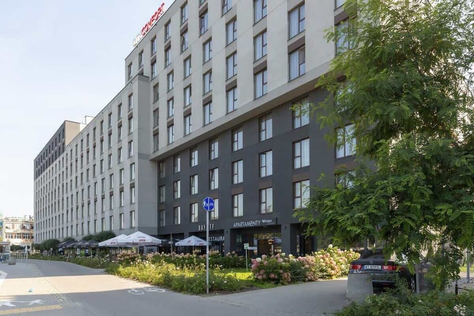 An exterior view of the building, surrounded by greenery and a well-maintained sidewalk, highlighting the modern architecture.

