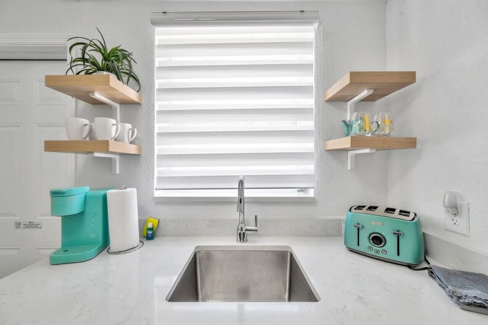 Sunny sink area w/ striped shade, open shelves, and cheerful turquoise accents