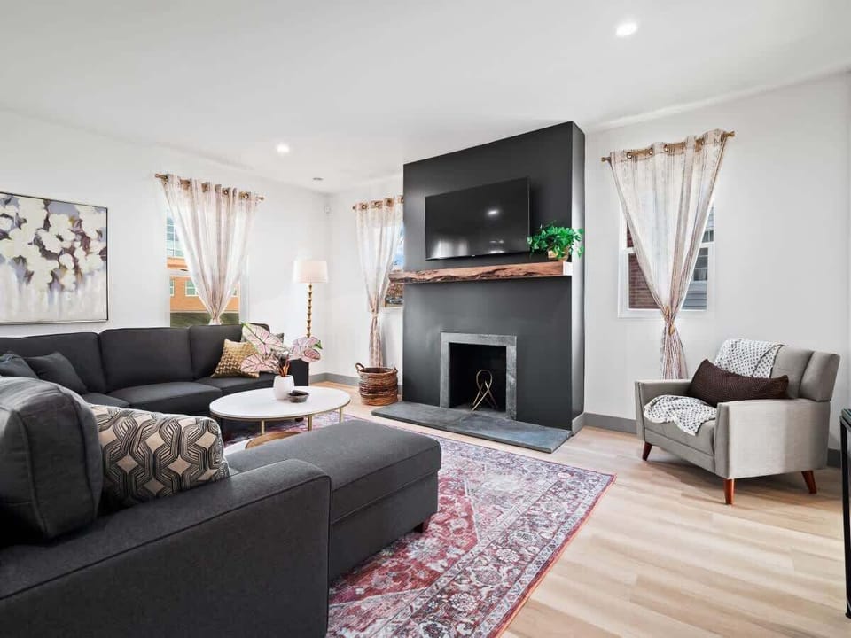 - Bright living room with sectional sofa and flat screen TV   - Cozy fireplace accent wall with wood beam detail   - Natural light and stylish decor for comfort  