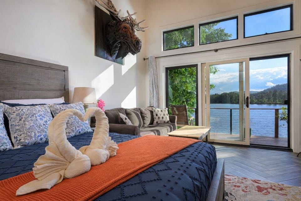 BEDROOM 1: Retreat upstairs to an oversized king suite where a plush bed, pullout sofa sitting area, soaring ceiling, & private balcony access create a peaceful haven above the water.