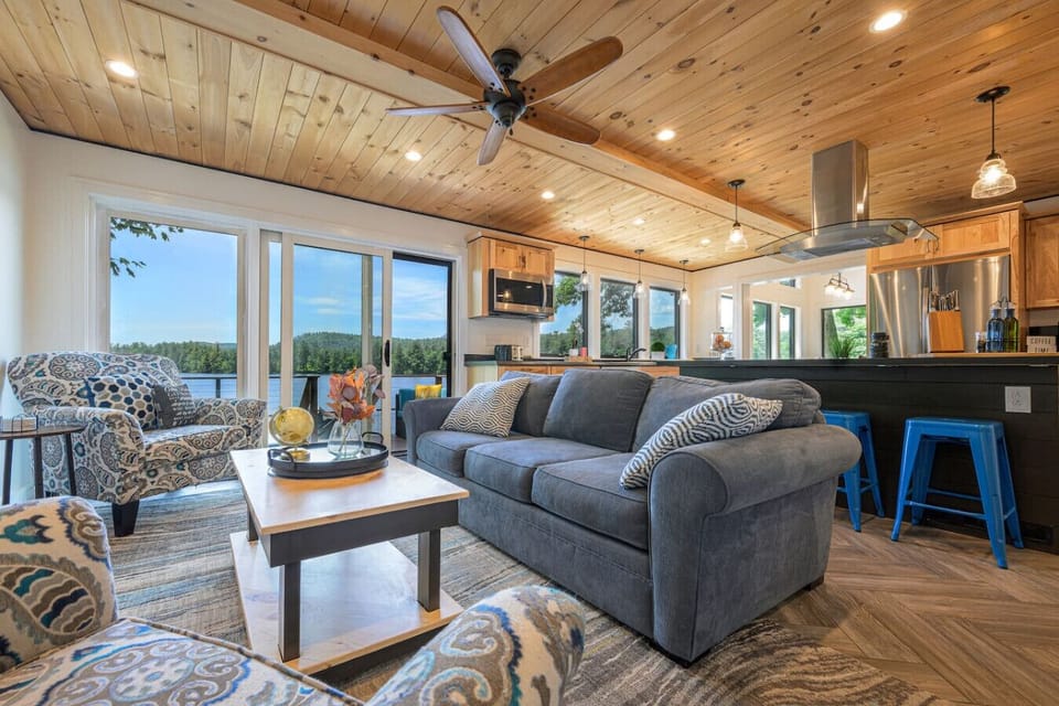 Your retreat begins in a light-filled living room where panoramic water views, warm natural wood, & generous seating invite everyone to settle in, reconnect, & stay awhile. *Now featuring Kuka accent seating in mellow steel blue.*